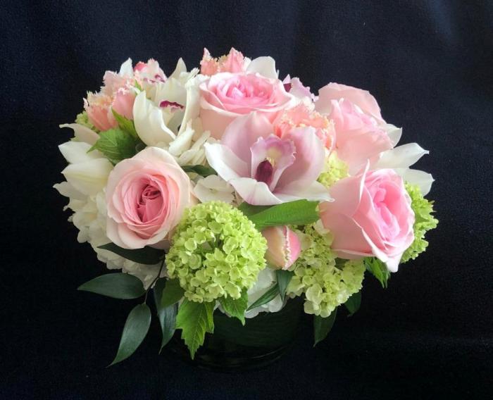 Pink and white spring bouquet of roses, orchid, tulips, and hydrangeas set against dark background.
